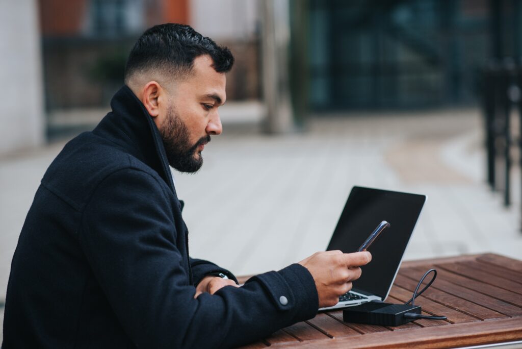 Man in black coat using mobile phone and laptop