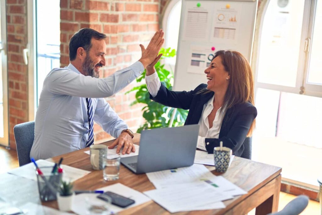 Two smiling middle-aged business workers high five, as they close an MCA deal.