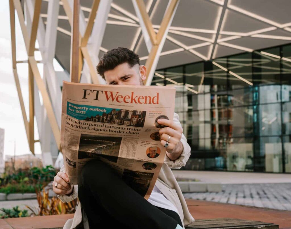 Young man reading Financial Times Weekend Edition in an urban setting.