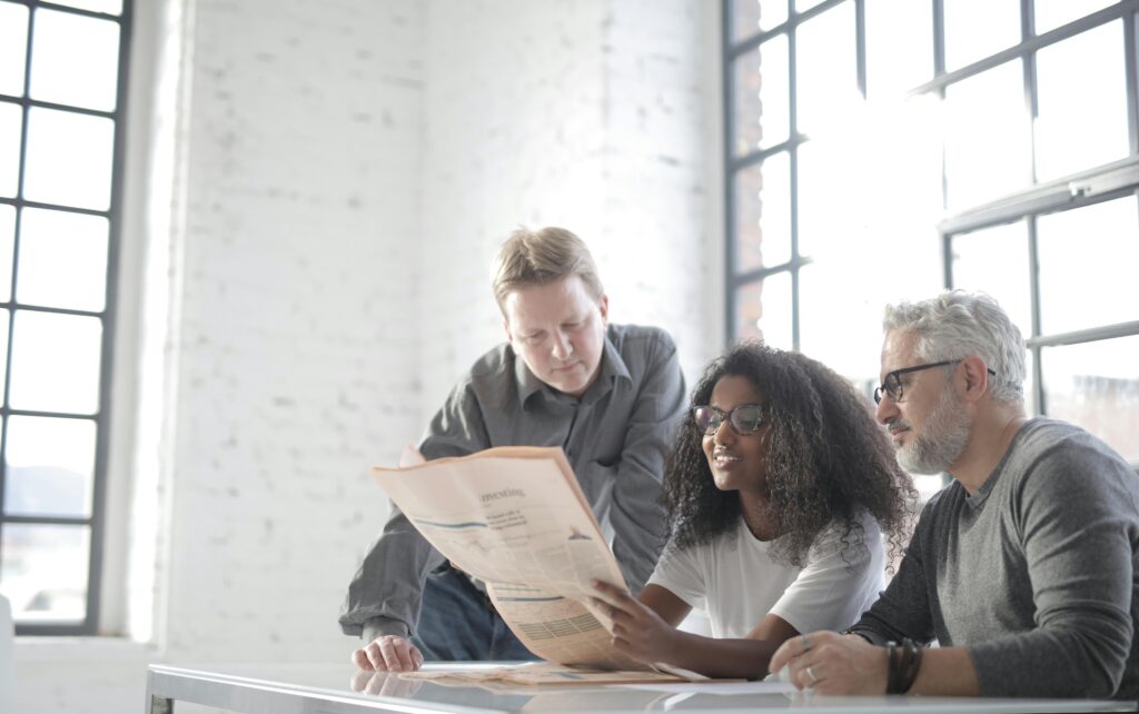 Three entrepreneurs look at a newspaper in a loft-style room with high ceilings and large windows.